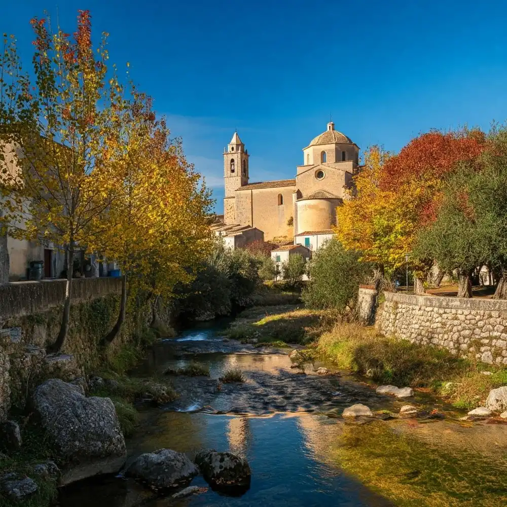 Paesaggio autunnale nel borgo di Gadona, alberi dalle foglie rosse circondano il fiume che raggiunge il centro storico