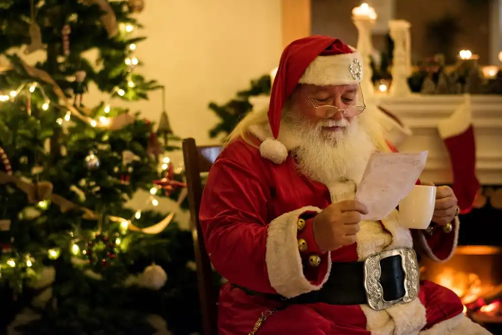 Babbo Natale che legge una letterina a casa sua, vicino ad un camino e mentre bene un caffe