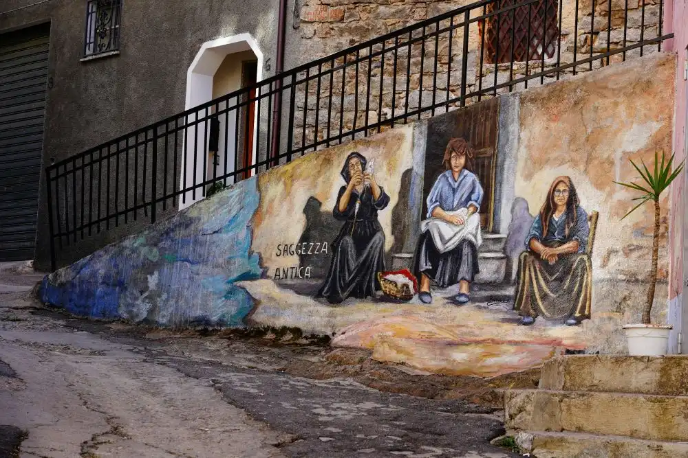 Un murales con tre signore con i vestiti classici sardi a Orgosolo in Sardegna, dove appare anche la scritta sagezza antica