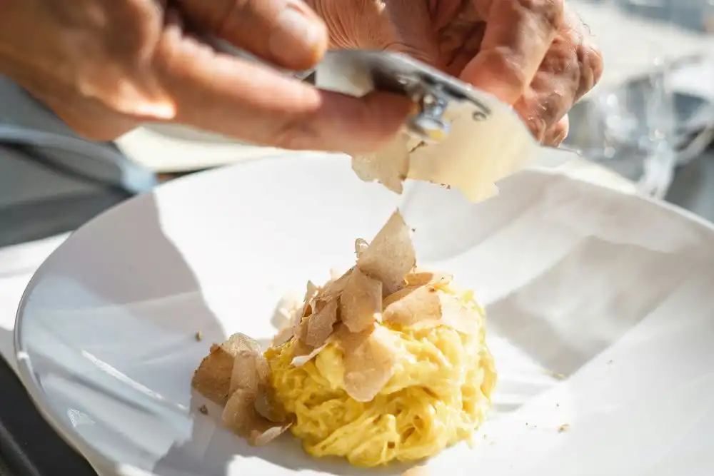 Piatto di pasta fresca su piatto pianco,una mano gratta il tartufo bianco di Alba